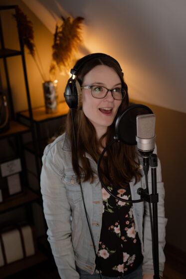 euer-persoenliches-lied-song-schreiben-lassen-hannah-stienen-(c)studiolaecheln-3 Hannah Stienen steht mit Kopfhörern auf vor einem Mikrofon und singt. Man könnte meinen, sie nimmt (Demo)Gesangsspuren für ein persönliches Lied auf.