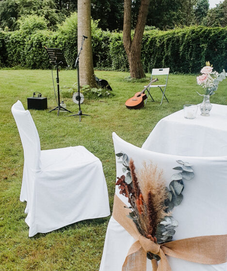lieder-freie-trauung-hannah-stienen-hochzeitssaengerin Freie Trauung auf einer Wiese: Blick von den Stühlen des Brautpaares auf die Stelle, wo die Musikerin steht: Gitarre, Verstärker, Mikrofonständer und Mikrofon.