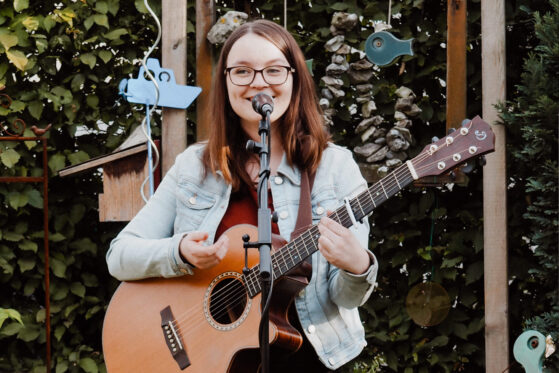 wohnzimmerkonzert-hannah-stienen-2021 Hannah Stienen während eines Auftritts bei einem Kartenkonzert mit Gitarre und Mikrofon.