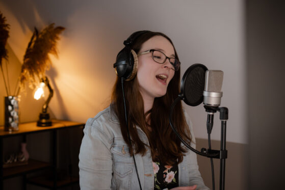 online-gesangsunterricht-hannah-stienen-(c)-studiolaecheln Hannah Stienen steht vor einem Mikrofon mit Popschutz und singt.
