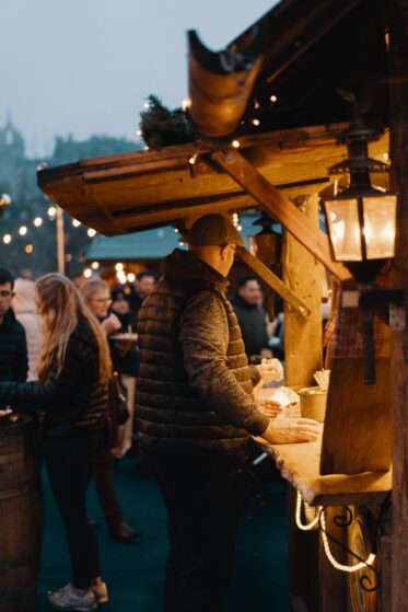 weihnachtsfeier-ideen-3 Man sieht, wie Menschen bei einer Bude auf dem Weihnachtsmarkt anstehen.