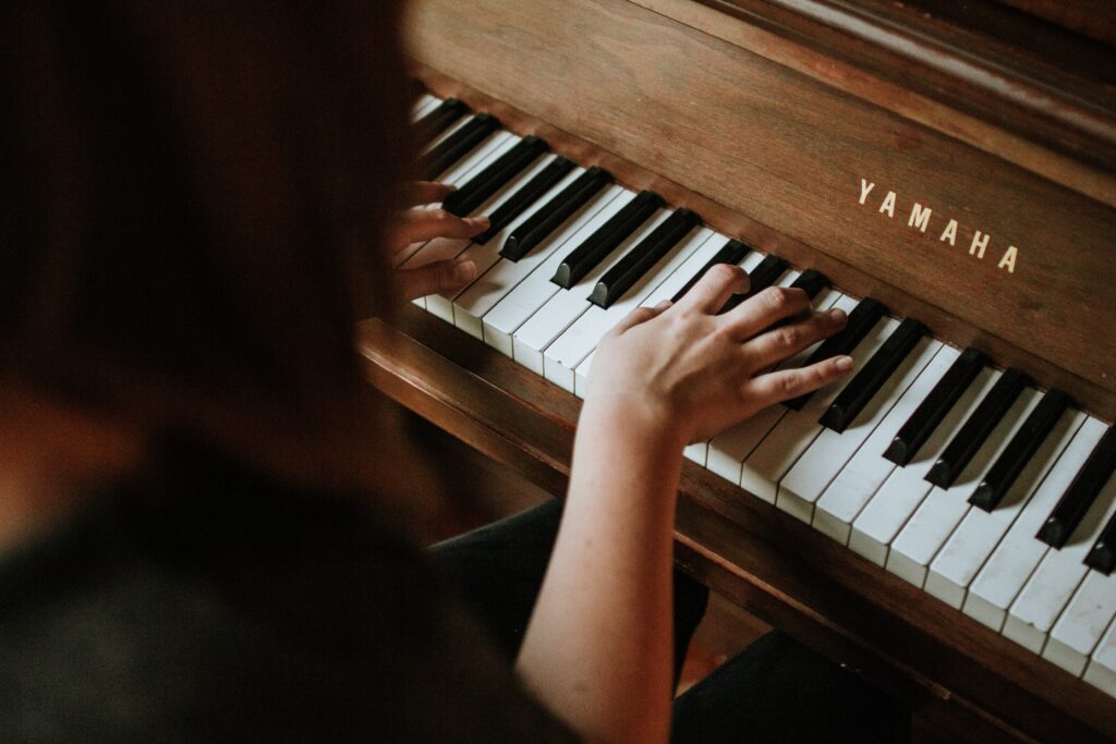 Blick von oben: Jemand spielt Klavier. Der Fokus liegt auf den Händen auf den Klaviertasten.
