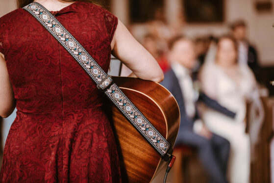 Hannah steht mit der Gitarre in der Kirche und singt Lieder für die kirchliche Trauung eines Brautpaares.