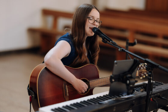 saengerin-zur-taufe-hannah-stienen-(c)-alina-buchholz Hannah Stienen steht mit ihrer Gitarre in einer Kirche und singt.
